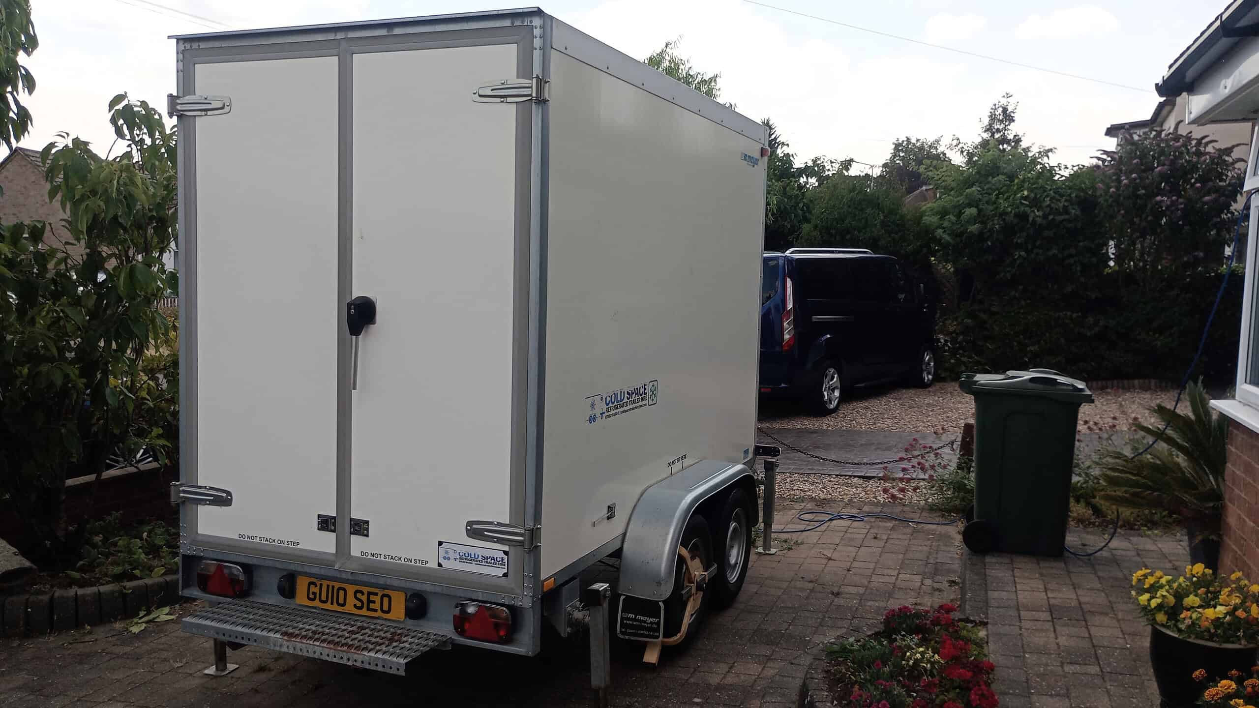 White refrigerated trailer parked in a residential driveway with greenery.